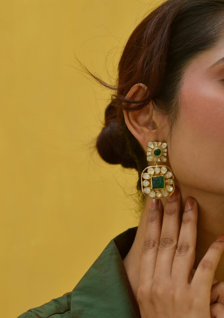 Close-up of a woman's hand showcasing a luxurious gold and emerald earring.